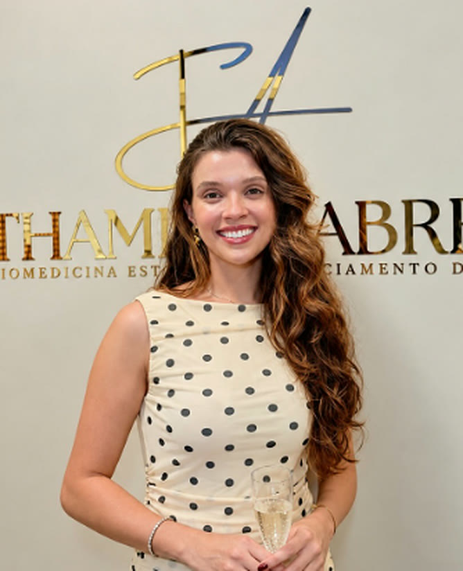 Thamires Abreu sorrindo em frente ao logo do consultório